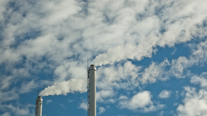 metal pipes of the plant against the blue sky, white smoke comes out of the pipes