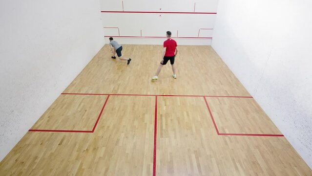 Professional athletes play squash striking ball in court