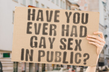 The question " Have you ever had gay sex in public? " is on a banner in men's hands with blurred background. Unlawful. Instruction. Intercourse. Illegal. Love. Prohibit. Healthy. Immoral. Behavior