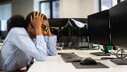 African young woman sitting at her desk clutching her head. 