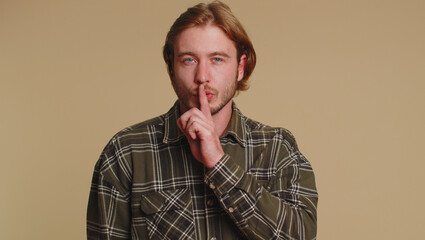 Obraz premium Shh be quiet please. Portrait of bearded adult man 20 years old presses index finger to lips makes silence gesture sign do not tells secret. Young adult handsome guy posing on beige studio background