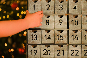 advent calendar in vintage style and childs hand near Christmas tree with glowing garland on...