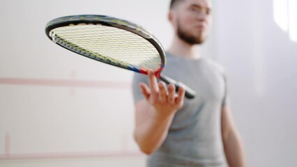 Bearded athlete spins racket on index finger in squash court