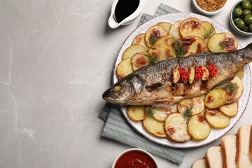 Plate with delicious roasted sea bass fish and potatoes on light grey table, flat lay. Space for text