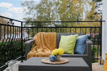 Colorful pillows, soft blanket and yellow chrysanthemum flowers on rattan garden furniture outdoors