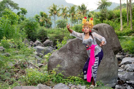 Balinese dancer woman outdoors with gold headdress and fan with a large stone in the background