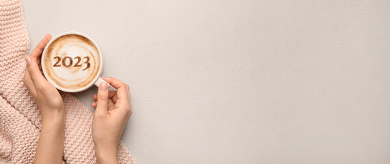 Female hands with cup of hot coffee and figure 2023 on light background with space for text