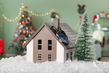 Model of house with key, Christmas tree and snow in room. Concept of real estate