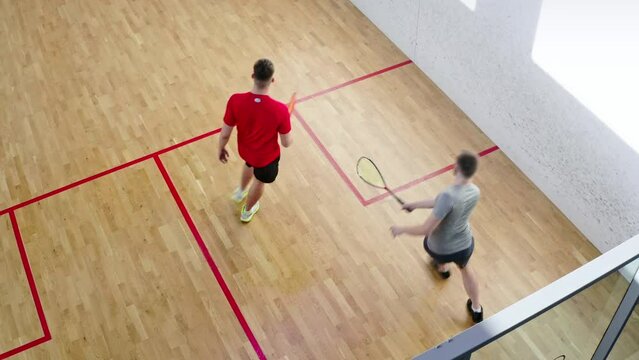 Couple of men play squash on playground with white walls