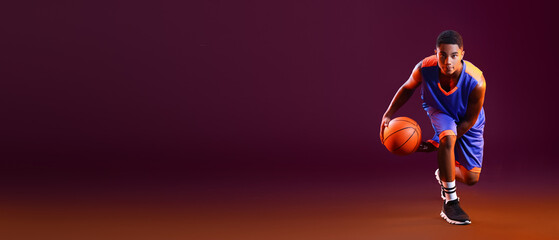 Young African-American basketball player on dark color background with space for text