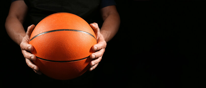 Basketball player holding rubber ball on dark background with space for text