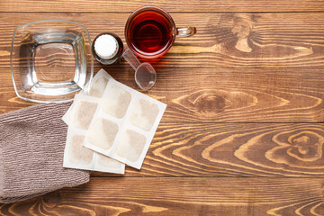 Mustard plasters with towel, bowl of water, tea cup and cough syrup on wooden background