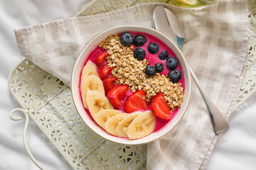 Bowl of tasty granola with yogurt and fruits on bed