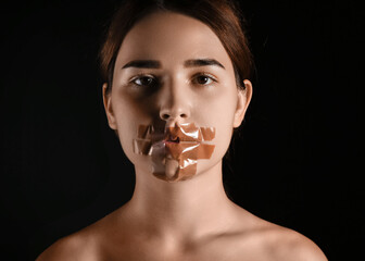 Young woman with taped mouth on dark background. Censorship concept