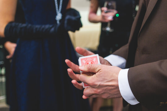 Magician illusionist with a deck of cards showing card tricks focus in front of wealthy rich guests on party event wedding celebration, juggler show, prestidigitator performance on a stage