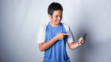 asian guy wearing tshirt looks suprised at the good news he received from his smartphone isolated white background