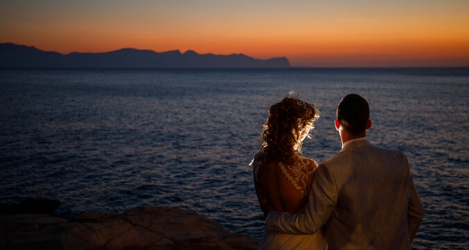 foto che ritrae coppia di sposi in una silhouette da dietro durante un servizio fotografico matrimonialista al tramonto nello scenario di cala rossa a Terrasini in provincia di Palermo