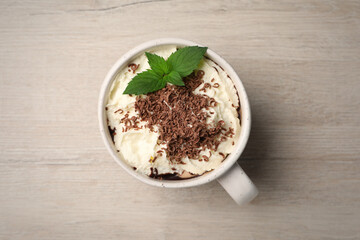Cup of delicious hot chocolate with whipped cream and mint on white wooden table, top view