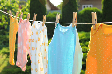 Clean baby onesies hanging on washing line in garden. Drying clothes