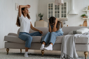 Obraz premium Communication problems between parents and teens. Exhausted parent can not deal with teenage daughter attitude, parental burnout. Teen girl covering ears with hands not to listen mom, sitting on sofa