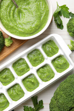 Broccoli puree in ice cube tray and ingredients on white wooden table, flat lay. Ready for freezing