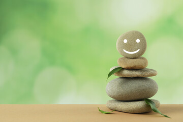 Stack of stones with drawn happy face and green leaves on table against blurred background, space...