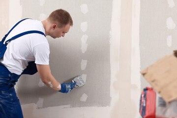 Man plastering wall with putty knife indoors. Home renovation - obrazy, fototapety, plakaty