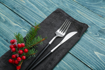 Napkin with cutlery and fir branch on color wooden background, closeup