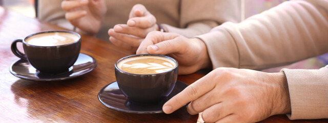 People with cups of aromatic coffee at wooden table, closeup. Banner design