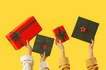 Women with Christmas gift boxes on yellow background