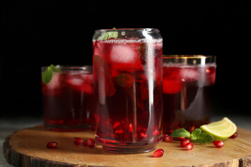 Wooden board with glasses of cold pomegranate juice on dark background, closeup