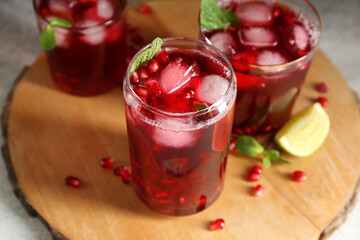 Wooden board with glasses of cold pomegranate juice on table, closeup