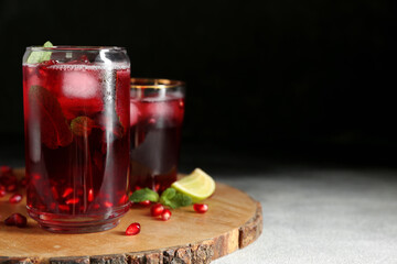 Wooden board with glasses of cold pomegranate juice on dark background, closeup
