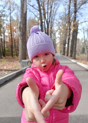 Cute Little expressive girl makes funny faces in autumn park