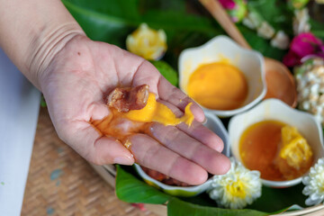 An elderly Asian woman receives a pain-relieving massage by a herbal therapist in a traditional Thai position.