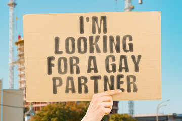 The phrase " I'm looking for a gay partner " is on a banner in men's hands with blurred background. Love. Behavior. Sensual. Affection. Desire. Erotic. Sexy. Orgasm. Ass. Intimacy. Gender