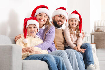 Happy family in Santa hats sitting on sofa at home
