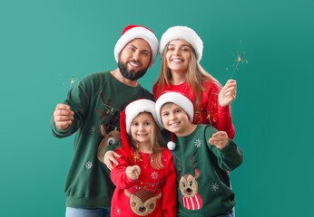 Happy family in Santa hats with Christmas sparklers on green background
