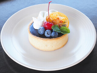  small cake with fruit and whipping cream on white plate.