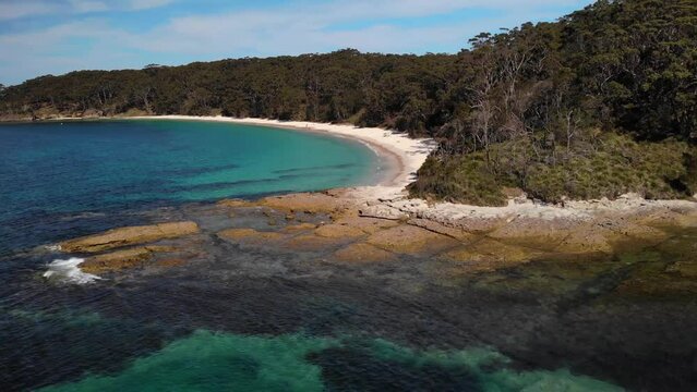 Aerial view overlooking the rocky shore of Jervis bay, New South Wales, Australia - rising, pull back, drone shot