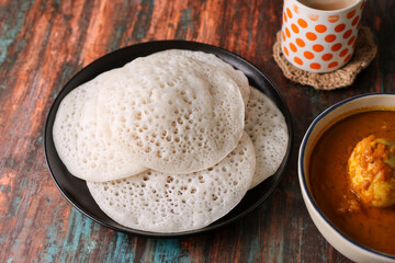 Appam pancake Kerala breakfast food Kadala curry egg curry chickpea Masala and tea, Christian breakfast on wooden background. fermented rice pan cake. Top view of Indian veg food.