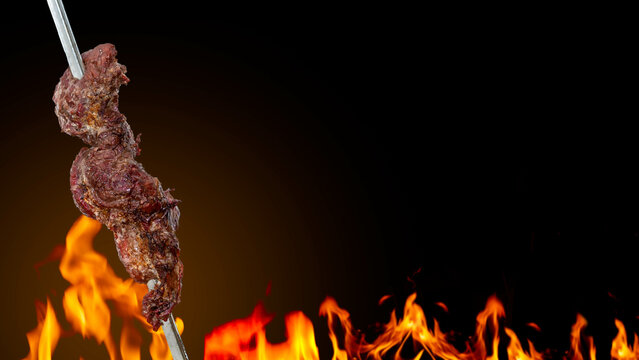 brazilian churrasco, traditional barbecue meat on skewer known as fraldinha assada, with fire on background and text area