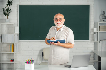 Senior teacher in the classroom on blackboard background. Old professor in high school or...