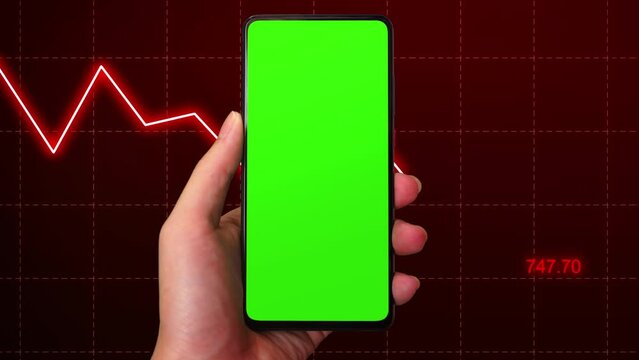 Hand businessman holding phone mobile on green screen on Stock markets Downtrend dynamic chart on dynamic red background. Concept of financial stagnation, recession, crisis, business crash