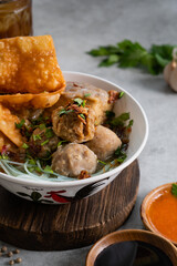 Bakso or indonesian meatball served with broth soup, tofu, noodle and deep fried wonton or dumpling on white bowl