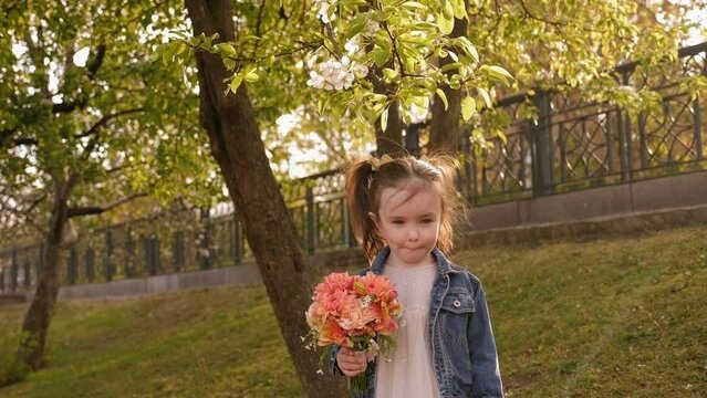 Portrait of a cute charming three-year-old girl with a bouquet of flowers in a spring Park in the sunset sun, she sniffs a bouquet of flowers.