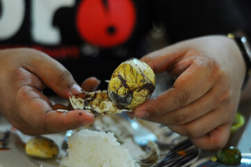 Crop photo of an unidentified Filipino man getting rid shell of a balut (fertilized duck egg)....