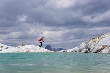 Hombre caminando por las rocas a la orilla de una laguna con un cielo nublado en Perú