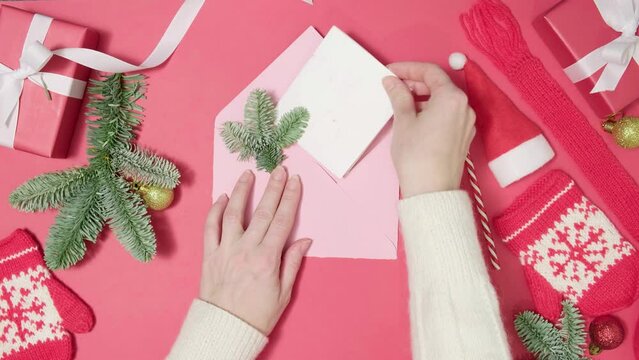 4K. Woman hand opening an envelope and taking out greeting letter Merry Christmas. Envelope with greeting card on table with Christmas gifts and pine tree. Merry Christmas and Happy New Year concept