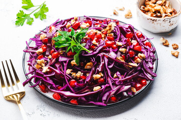 Vegan red cabbage salad with parsley, pomegranate seeds, walnuts and olive oil dressing on white kitchen table background. Healthy diet food. Top view